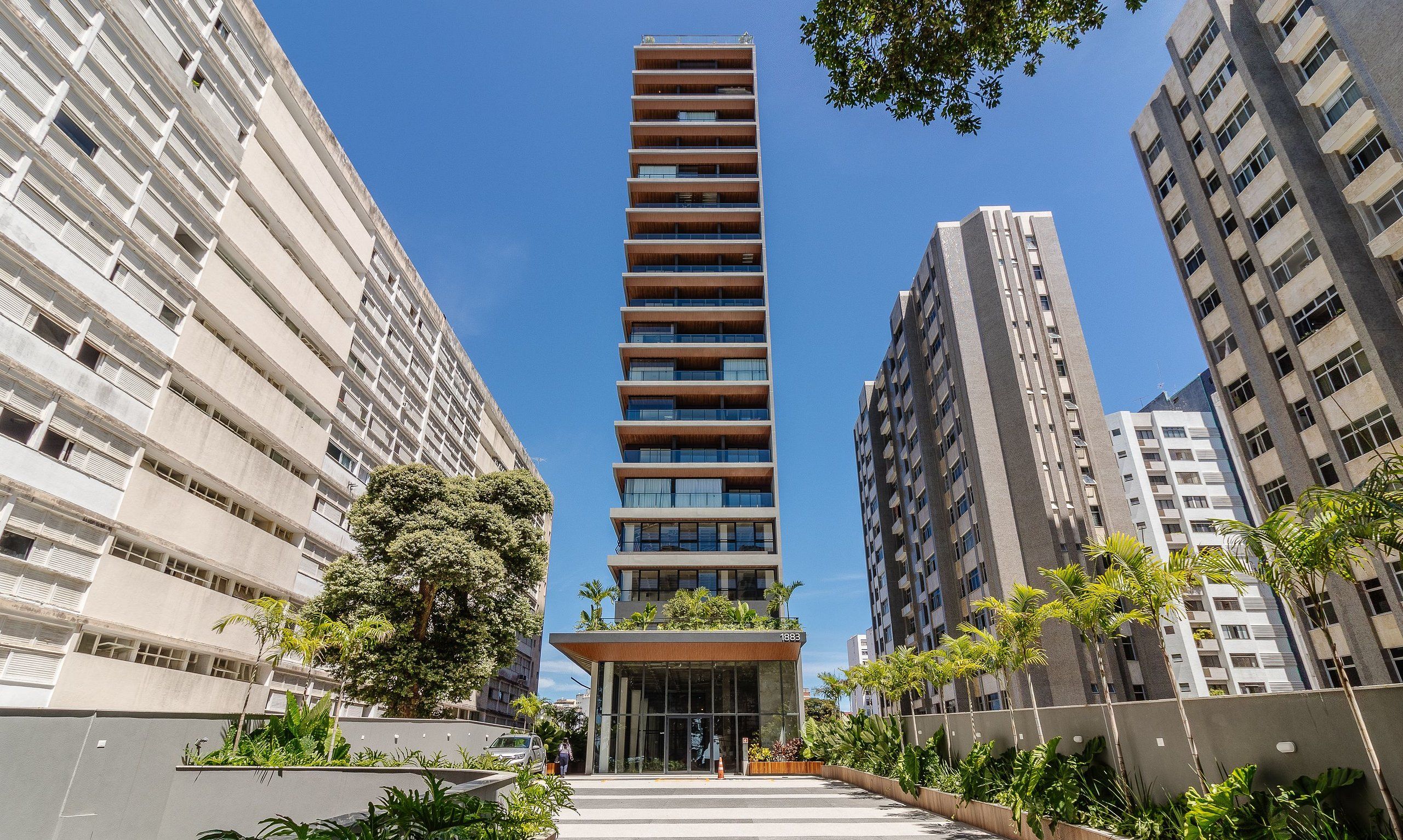 Een modern hoog gebouw met een centrale ingang, omringd door andere hoge gebouwen.