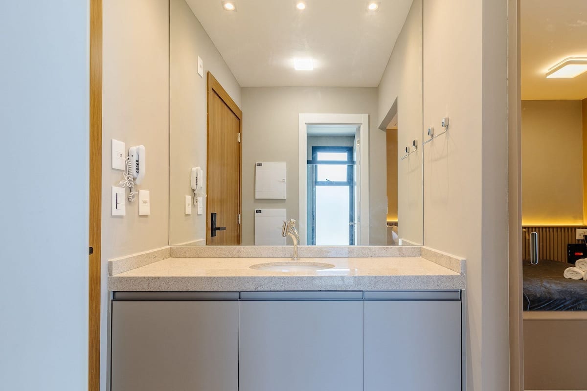 A modern bathroom with a large mirror, a sink, and a door leading to a bedroom.