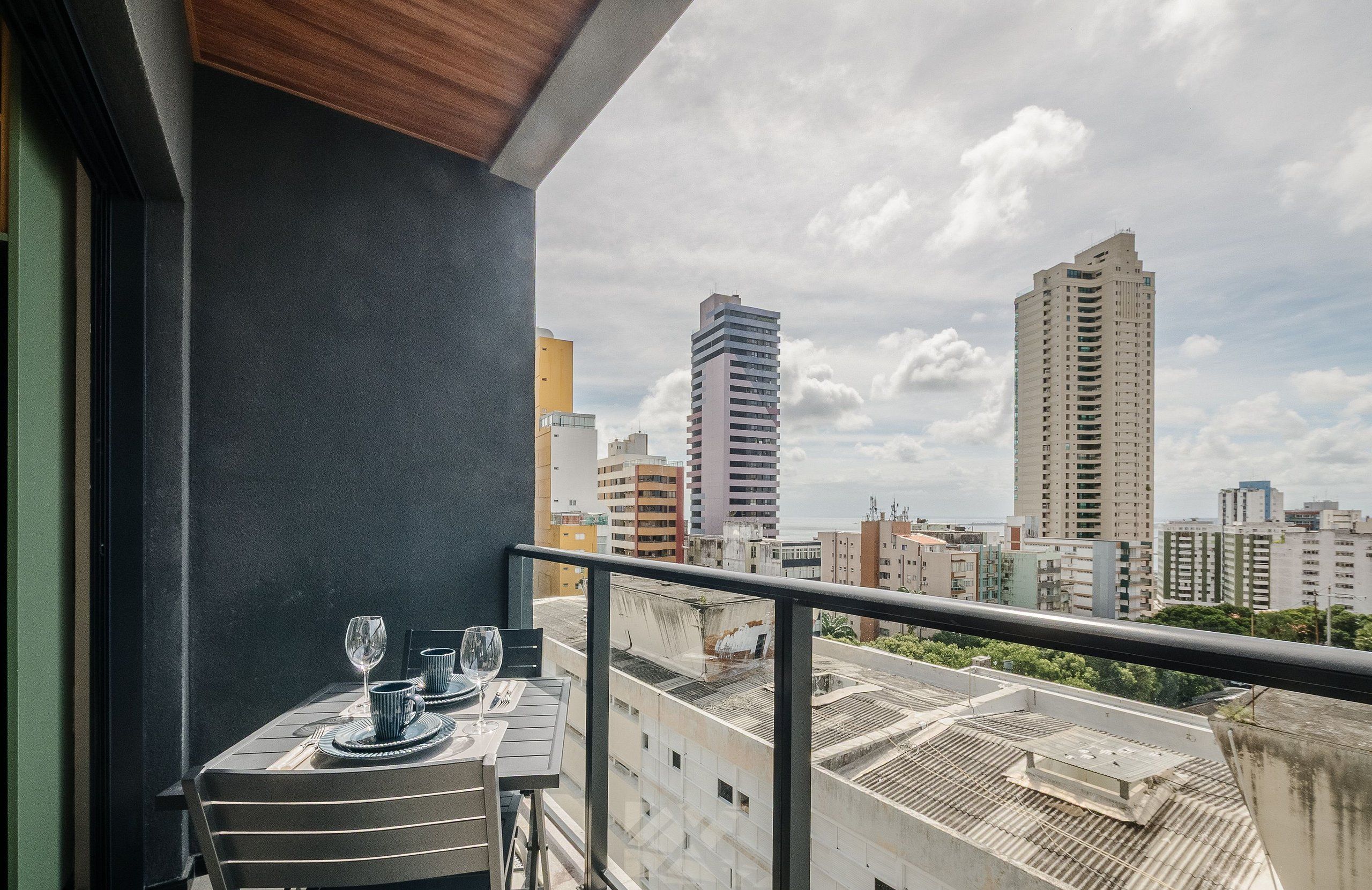A balcony with a table set for dining, overlooking a cityscape with multiple high-rise buildings.