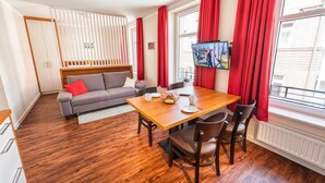 Ein modernes Wohnzimmer mit einem Holzespeisetisch, einem grauen Sofa und roten Vorhängen.