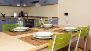 A dining table set with white plates, green chairs, and two wine glasses. - Milano 27 - Two Bedroom Apartment, Sleeps 4 (Bormio)