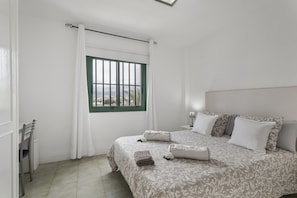 A bedroom with a bed, pillows, a nightstand, a chair, a window with a view, and a curtain. - Vacation 'Costa Serena' with Mountain View, Shared Pool and Wi-Fi (Arona)