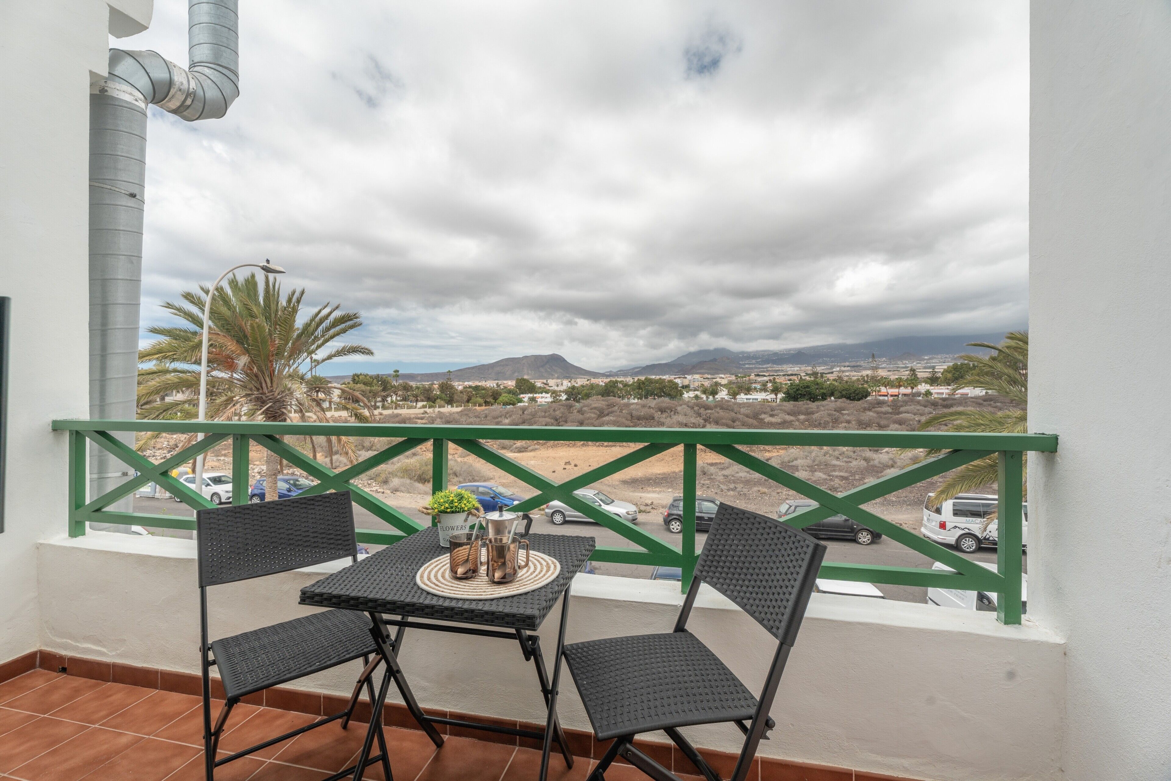 Un balcon avec une table et des chaises, une vue sur le paysage urbain et une rambarde verte.