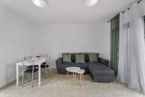 A modern living room with a grey sectional sofa, a white dining table with chairs, and a small white side table.