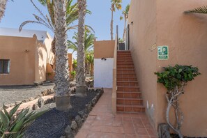 A courtyard with palm trees, a staircase, and a building with a sign. - Vacation 'Viento Azul' with Shared Pool, Wi-Fi and Air Conditioning (Corralejo)