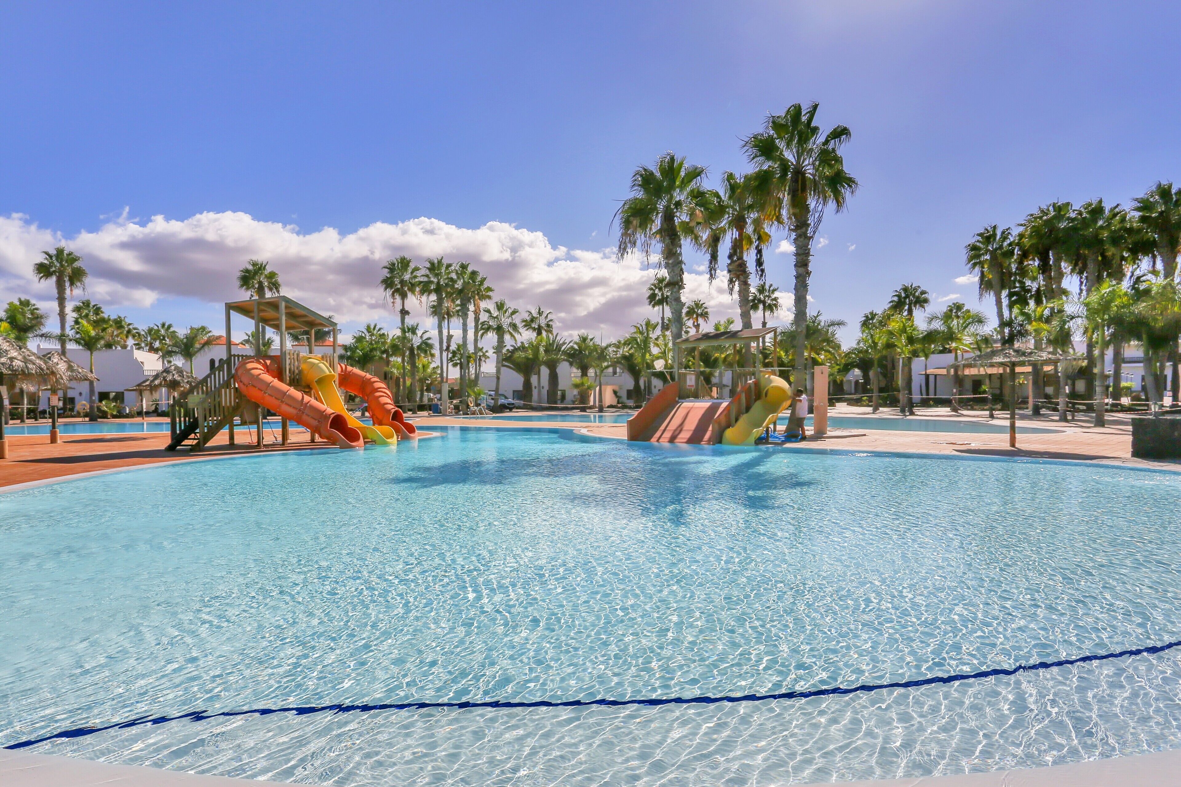 Ein Schwimmbecken mit Wasserrutschen, Palmen und blauem Himmel.