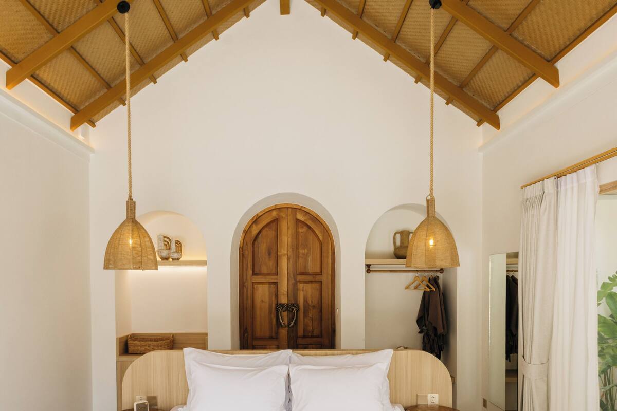 Een slaapkamer met een groot bed, houten balken in het plafond en hanglampen.
