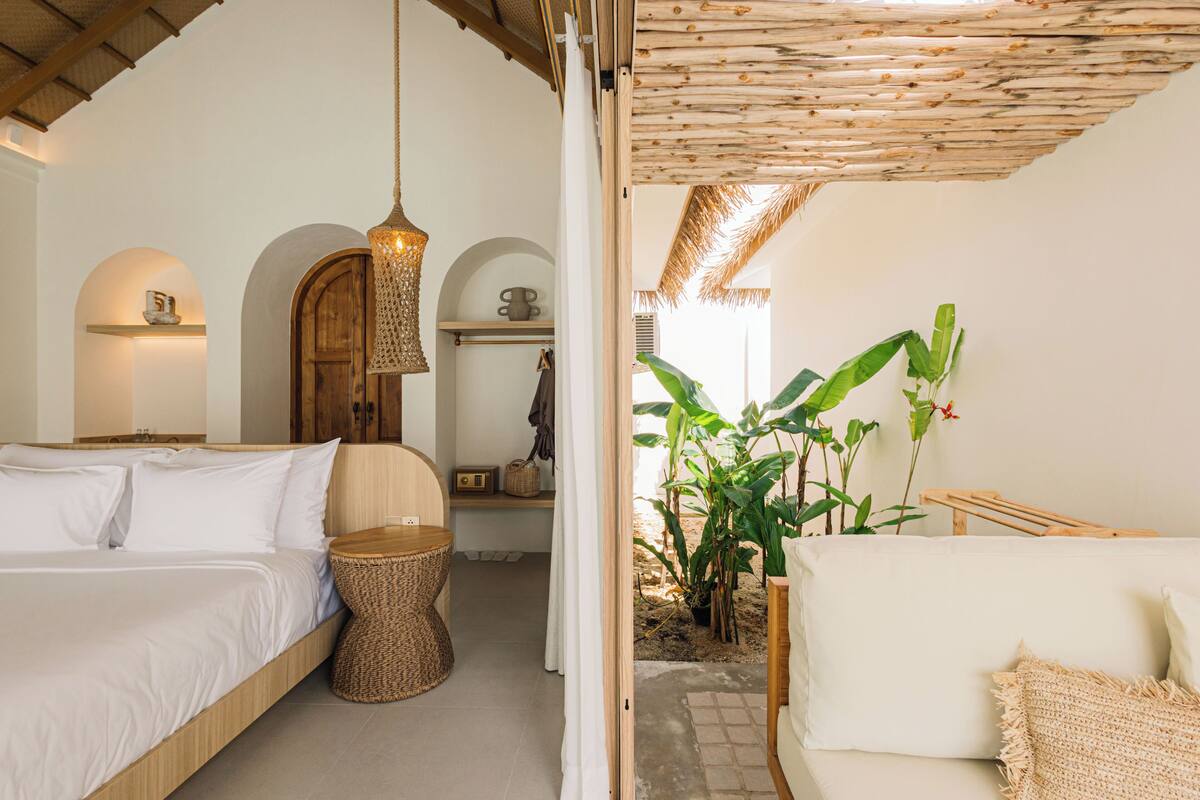 Een slaapkamer met een houten bed, een geweven nachtkastje en een hanglamp.