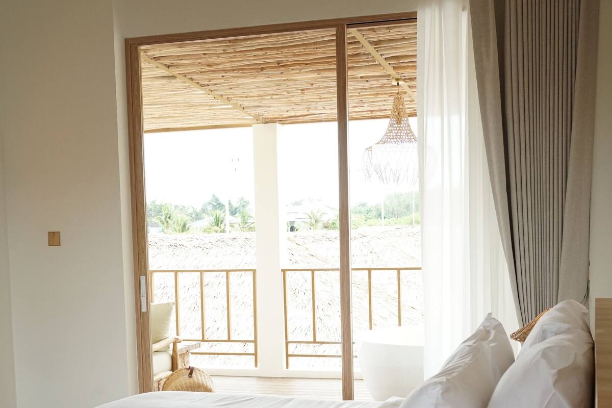 Een slaapkamer met een bed, nachtkastje met lamp, uitzicht op de omgeving via een schuifdeur en een balkon met een stoel.