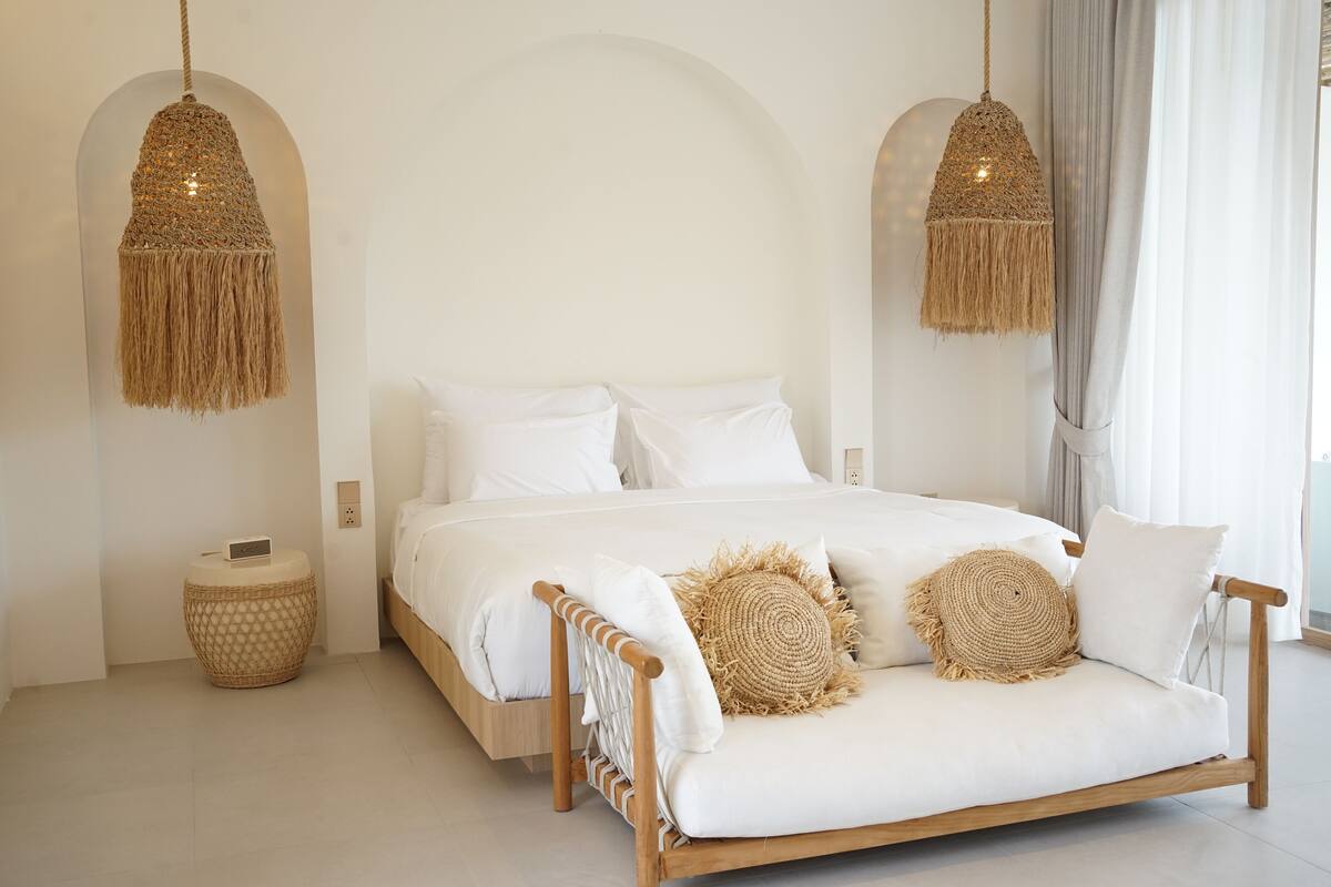 Een minimalistische slaapkamer met een houten bed, witte beddengoed en geweven decoratieve kussens.