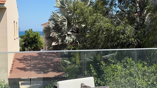 A balcony with a glass railing, outdoor furniture, and lush greenery.