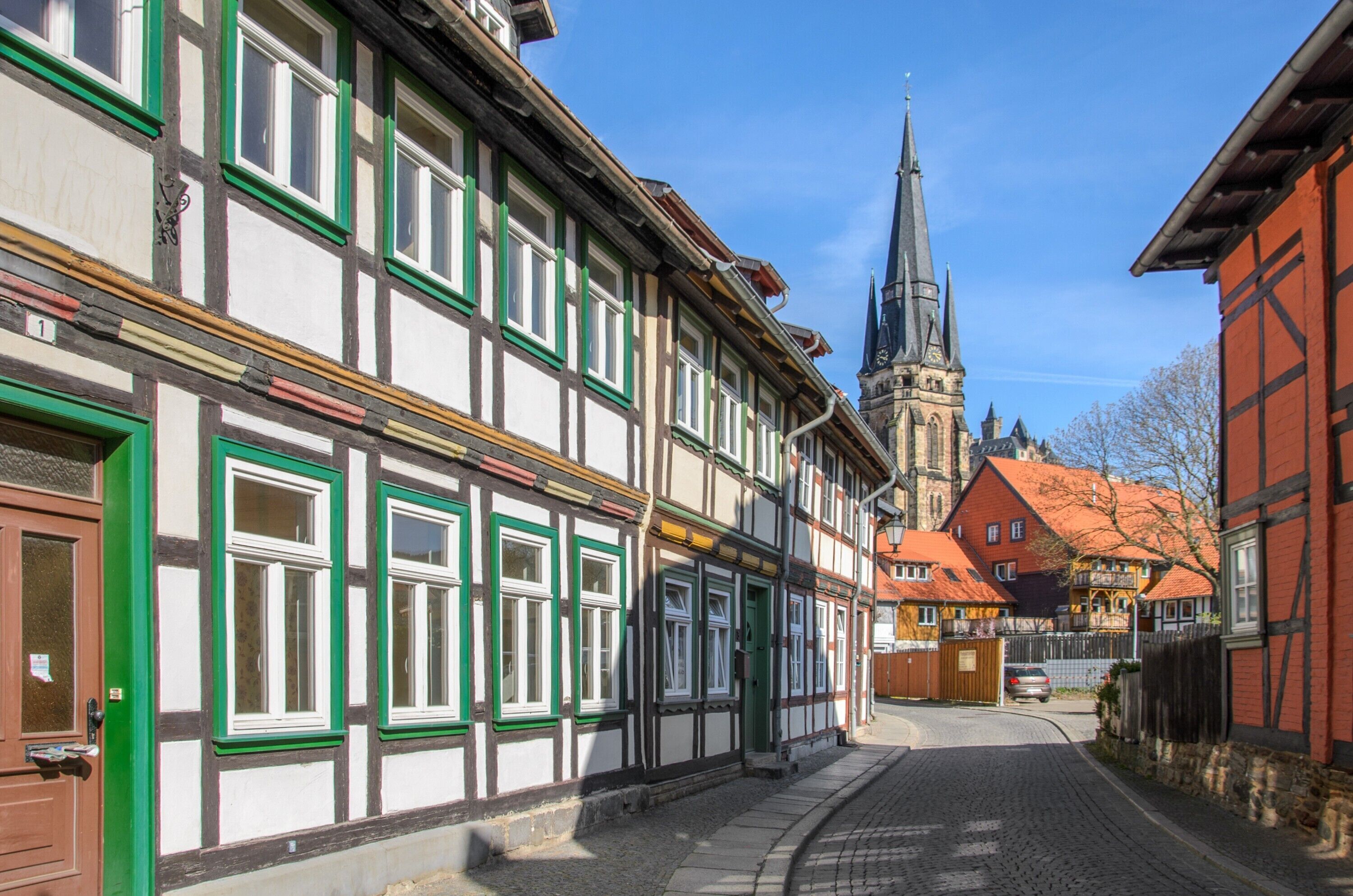 A narrow street with traditional half-timbered buildings, a church steeple, and cobblestone pavement.