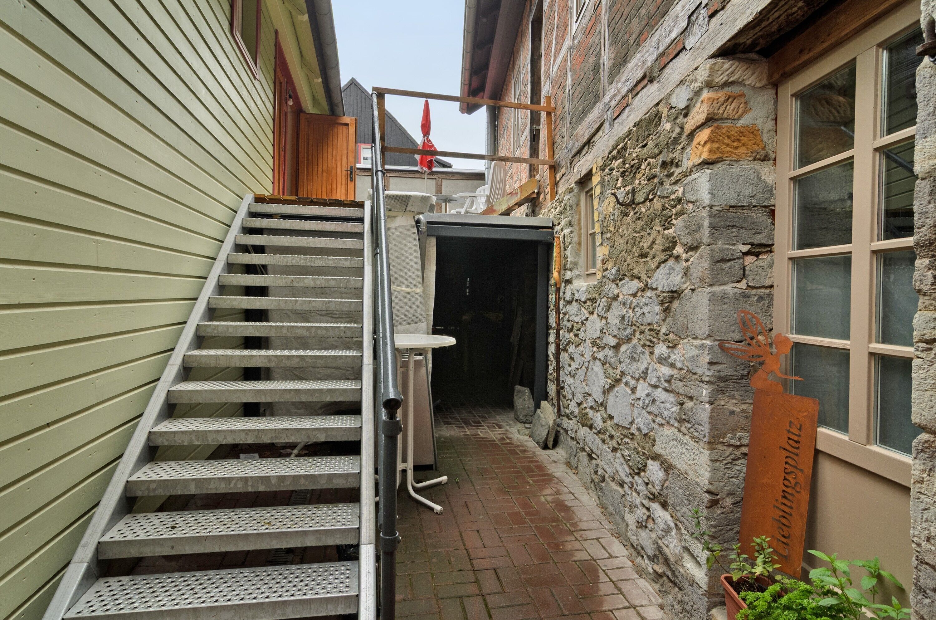 A narrow outdoor stairway leading to a covered entrance, a stone wall, and a metal sign.