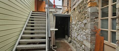 A narrow outdoor stairway leading to a covered entrance, a stone wall, and a metal sign.