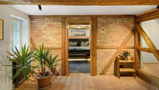 Una habitación con vigas de madera a la vista, pared de ladrillo, cama y una planta en maceta.
