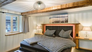 Un dormitorio con una cama grande, dos mesitas de noche, un ventanal con cortinas y una viga de techo de madera.