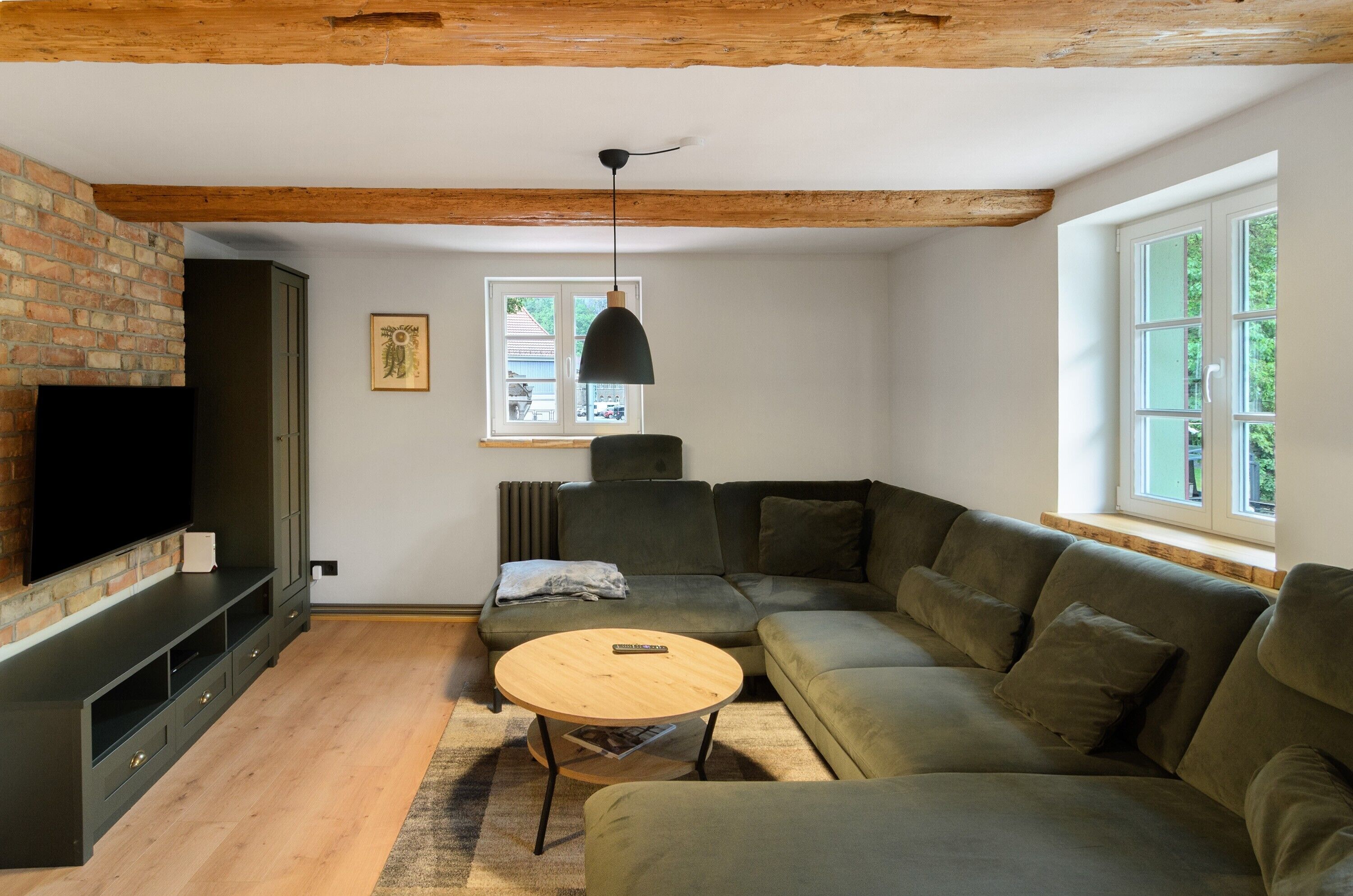 Una sala de estar con un sofá modular, un televisor en una pared de ladrillo, techo de madera y una ventana con vistas.