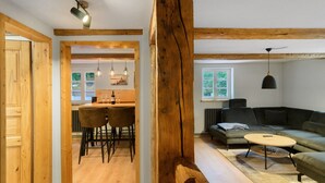 Amplia sala de estar con techo de madera, un sofá verde, una mesa de centro redonda y un comedor con sillas y una mesa.