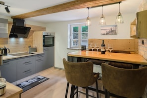 A modern kitchen with wooden beams, a built-in oven, and a dining area with two chairs and a table.