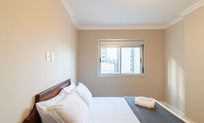 A hotel room with a single bed, a window with a view of buildings, and a small window with a view of the sky. - Apart With Barbecue 100m From the Beach Don0504 (Balneário Camboriú)