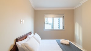 A hotel room with a bed, a window with blinds, and a towel on the bed.