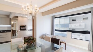 A modern kitchen with built-in appliances, a glass dining table, and a chandelier.