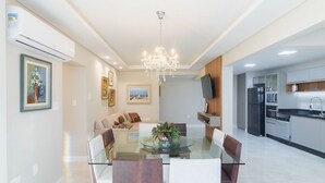 A modern dining area with a glass table, cushioned chairs, and a chandelier.