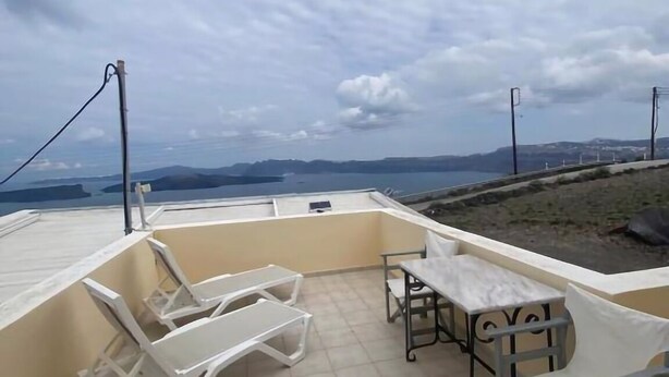A rooftop terrace with a table and chairs, a view of the sea, and a cloudy sky. - Aeolos Apartments (Santorini)