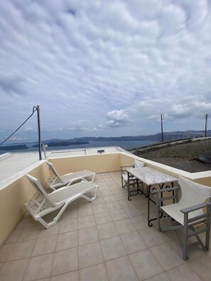 Une terrasse sur le toit, avec une table et des chaises, une vue sur la mer et un ciel nuageux.