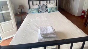 A bedroom with a bed, a nightstand, a lamp, and a fire extinguisher. - Aeolos Apartments (Santorini)