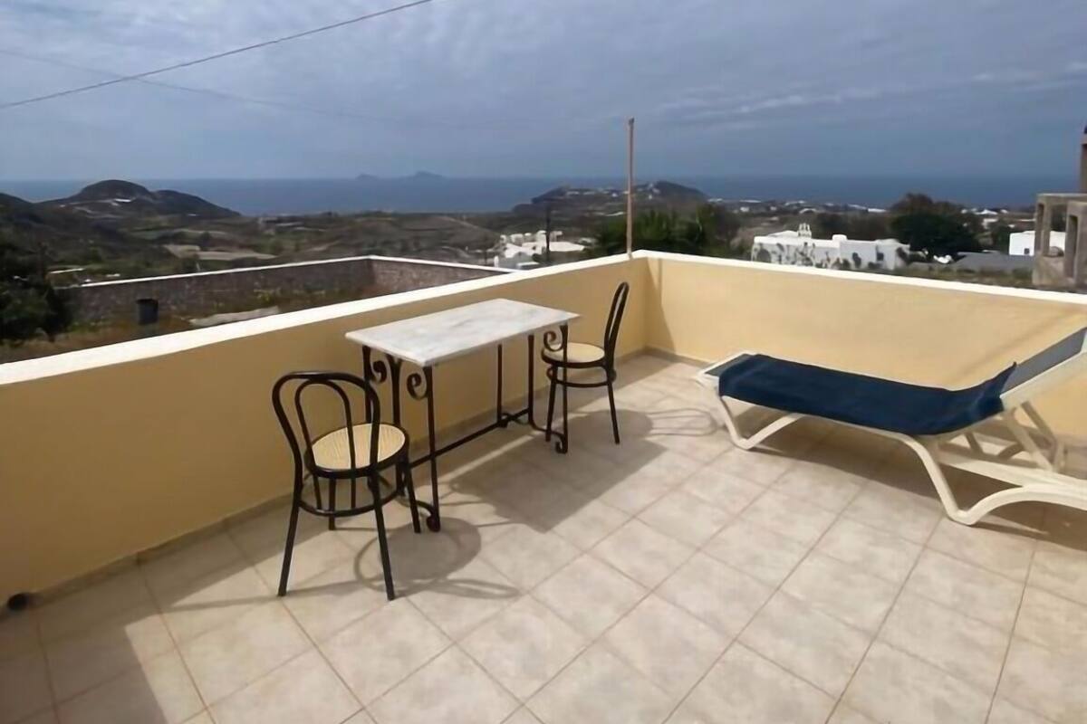 A balcony with a table and chairs, a sun lounger, and a view of the landscape.
