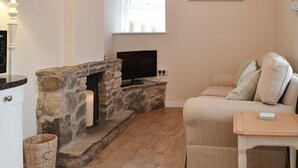 Un salon chaleureux avec une cheminée en pierre, un téléviseur à  écran plat fixé au-dessus, et un canapé confortable agrémenté de coussins.