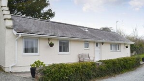 Une maison de plain-pied avec un toit en pente, des murs extérieurs blancs et un petit porche avec une chaise.