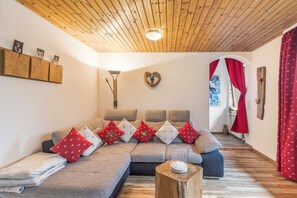 A cozy living room with a wooden ceiling, a sofa with patterned cushions, a heart-shaped decoration, and a vase on a wooden stool.
