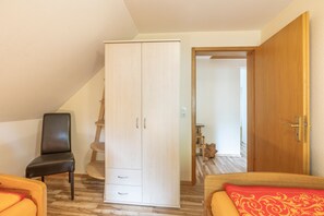 Een slaapkamer met een kledingkast, een stoel, een bed met een rood kussen, en een houten deur.