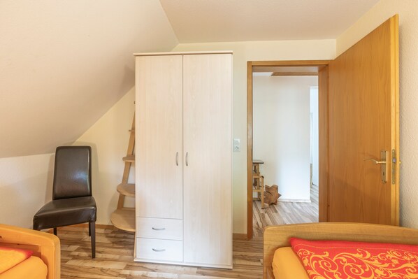 A bedroom with a wardrobe, a chair, a bed with a red pillow, and a wooden door.