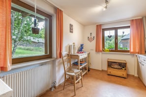 A room with a radiator, a wooden chair, a table with a kettle, and a window with curtains.