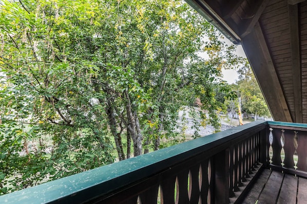 A wooden balcony with a view of dense green foliage and trees.