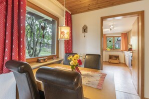 Een eetruimte met een tafel, stoelen en een raam met gordijnen.