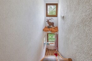 Een smalle trap met een houten leuning, een klein raam aan de bovenkant en een herten decoratie aan de muur.