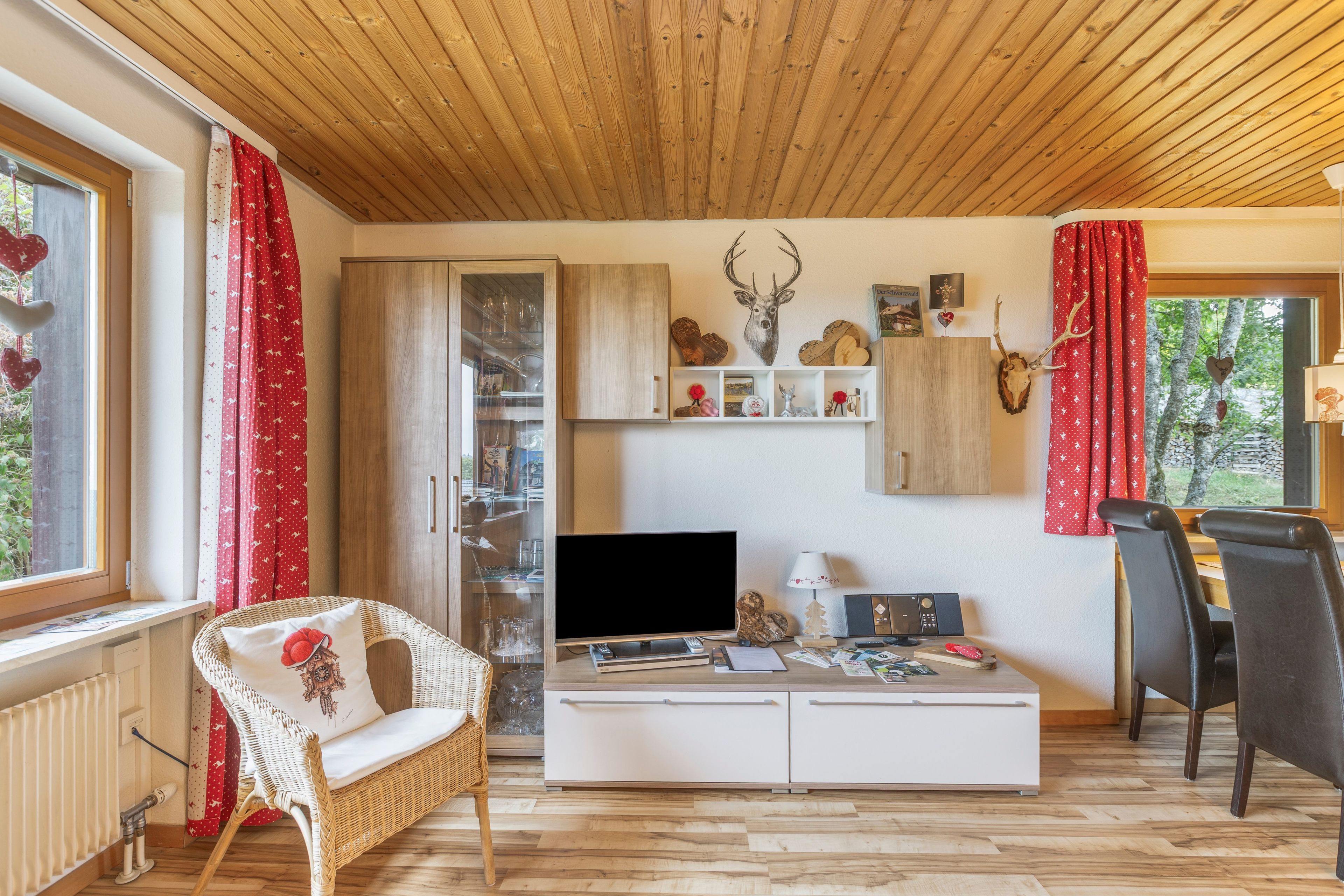 Una sala de estar acogedora con televisor, un mueble blanco, un sillón de mimbre y un comedor con mesa y sillas.