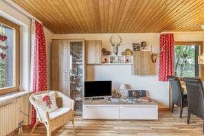 A cozy living room with a television, a white cabinet, a wicker chair, and a dining area with a table and chairs.