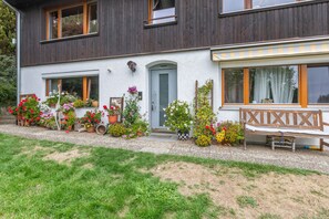 Une maison à deux étages avec un porche à l’avant, des plantes en pot et un banc en bois.