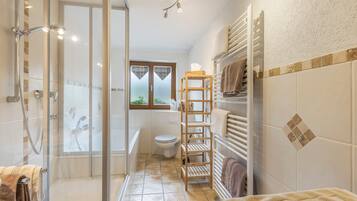 Un baño con cabina de ducha de vidrio, inodoro y estante de madera con toallas.