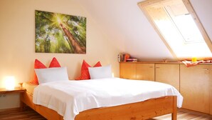 Ein Schlafzimmer mit einem hölzernen Bett, einem Oberlicht, einem Baumgemälde und einem Nachttisch mit Lampe.
