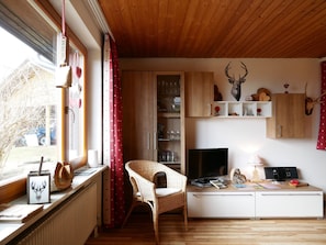 A cozy room with a wooden ceiling, a wicker chair, a TV, and a desk with various items. - Apartment 'Jurisch' with Shared Garden, Balcony and Wi-Fi (Dachsberg (Südschwarzwald))
