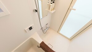 A modern bathroom with a bathtub, a towel rack, a mirror, and a shelf with toiletries.