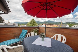 A rooftop terrace with a red umbrella, a table with a vase, and a blue-striped lounge chair.