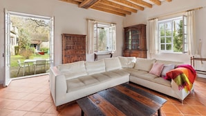 Un salon spacieux avec un grand canapé d’angle beige, une table basse en bois et une vue sur un jardin grâce à des portes ouvertes.
