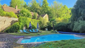 Une piscine entourée de verdure et d’un mur de pierre, avec des chaises longues et des parasols à proximité.